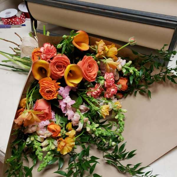 Bouquet of orange and pink flowers with trailing greenery on brown paper