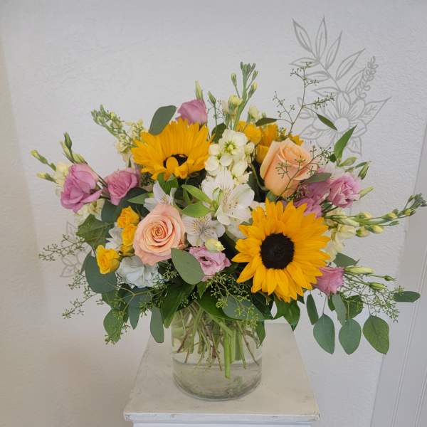 Mixed bouquet with sunflowers, roses, and white blooms in a glass vase