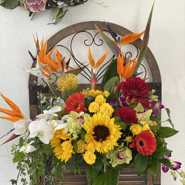 Tropical bouquet with sunflowers, orchids, and bright orange bird-of-paradise in a glass vase