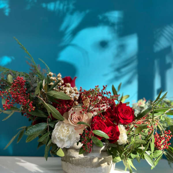 Red and white roses arranged in a low stone vase with berries