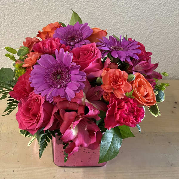 Pink and purple mixed flower arrangement in a square pink vase