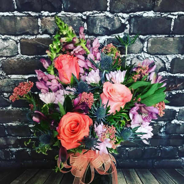 Bouquet of coral roses and purple flowers in a black vase with a ribbon