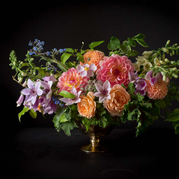 Mixed bouquet of pink, peach, and lavender flowers in a gold vase
