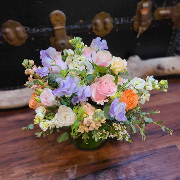 Pastel bouquet of roses and lavender flowers in a low green vase