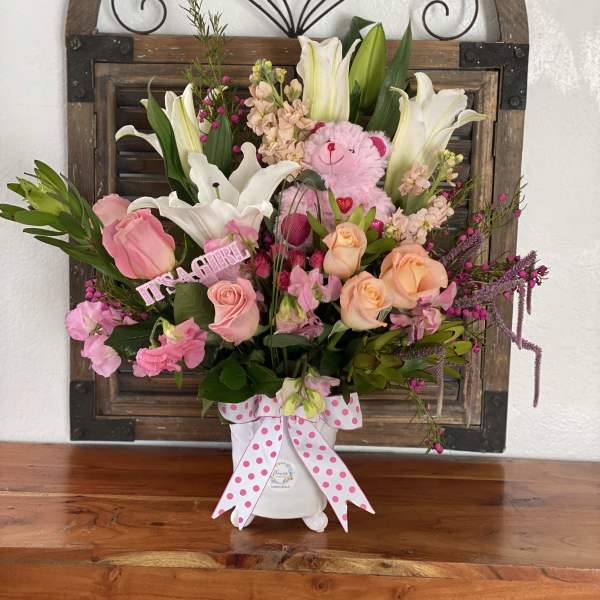 Pink and white floral arrangement with a teddy bear in a white vase