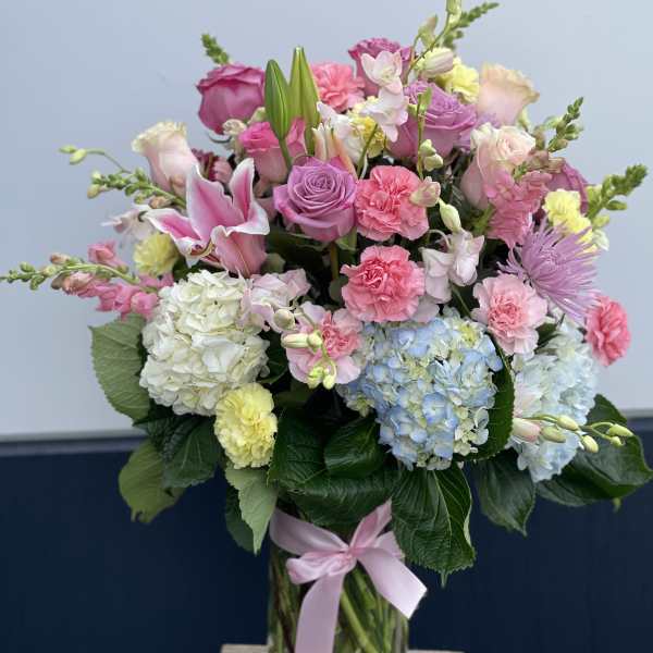 Mixed pastel bouquet in a glass vase with pink, blue, and white blooms