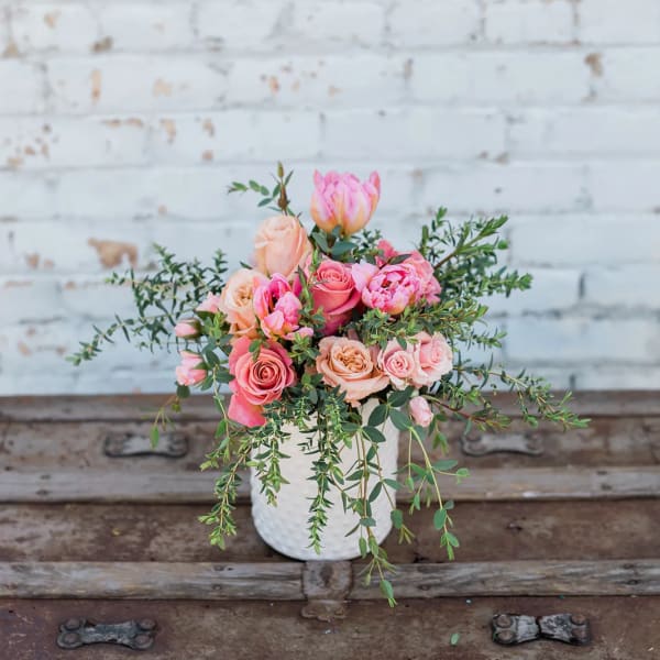 Pink and peach roses in a white vase with trailing greenery