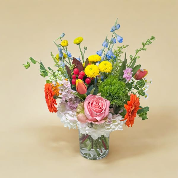 Mixed bouquet in a clear glass vase with pink, orange, yellow, blue, and white flowers