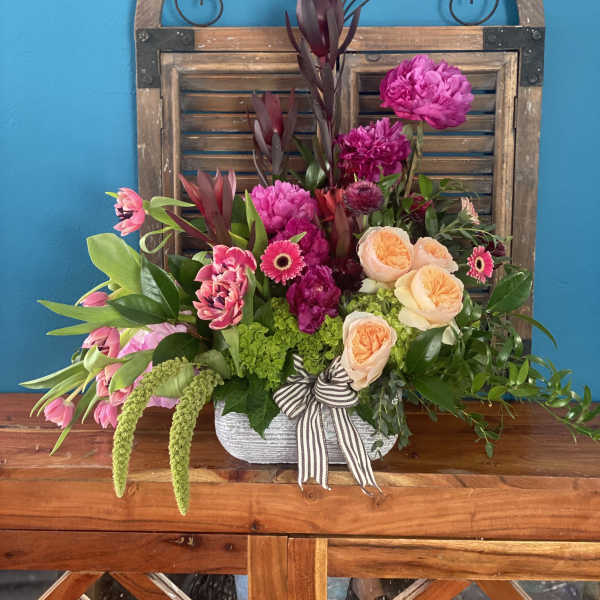 Mixed pink and peach floral arrangement in a white container with a striped ribbon
