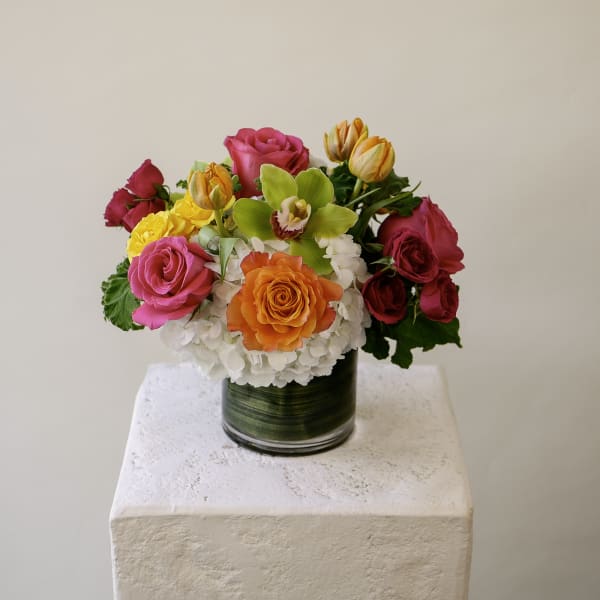 Bright arrangement of roses, tulips, hydrangea, and a green orchid in a green-lined glass cylinder vase