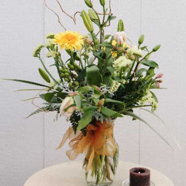 Tall mixed flower arrangement in a glass vase with a candle beside it