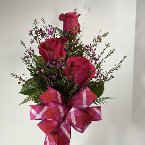 Pink roses in a clear vase with a large plaid ribbon bow