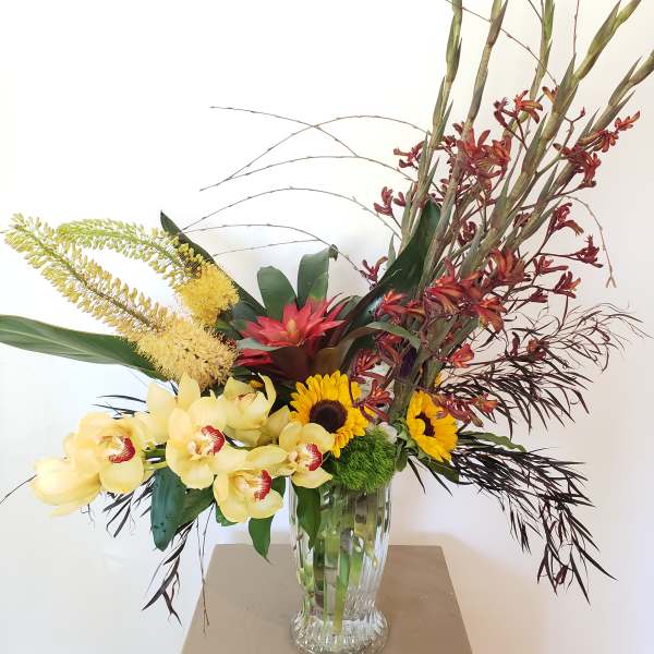 Tropical flower arrangement in a clear glass vase with orchids and sunflowers