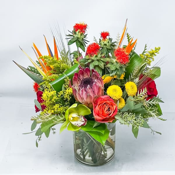 Mixed bouquet in a glass vase with protea, roses, orchids, and yellow blooms