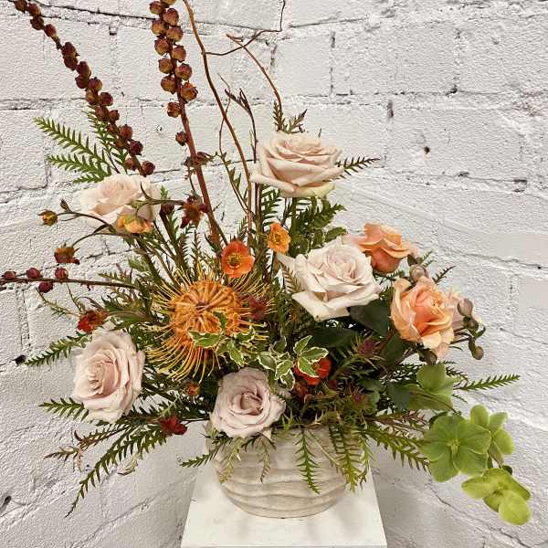 Mixed floral arrangement in a white vase with pale roses and orange blooms