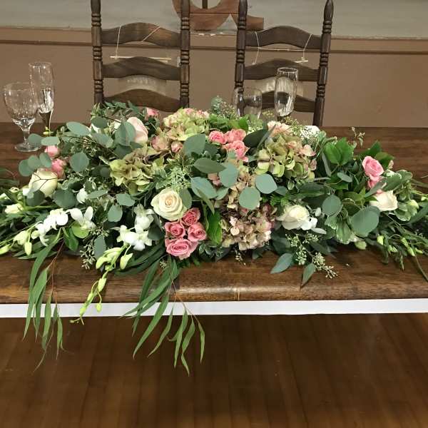 Low floral centerpiece with pink and white roses and greenery on a table
