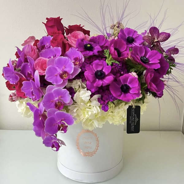 Pink and purple floral arrangement in a white hat box