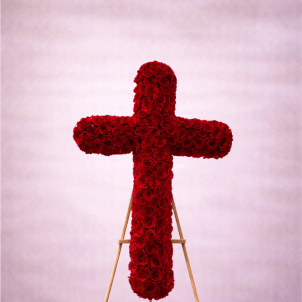 Standing cross of red roses on a wooden easel against a soft pink backdrop