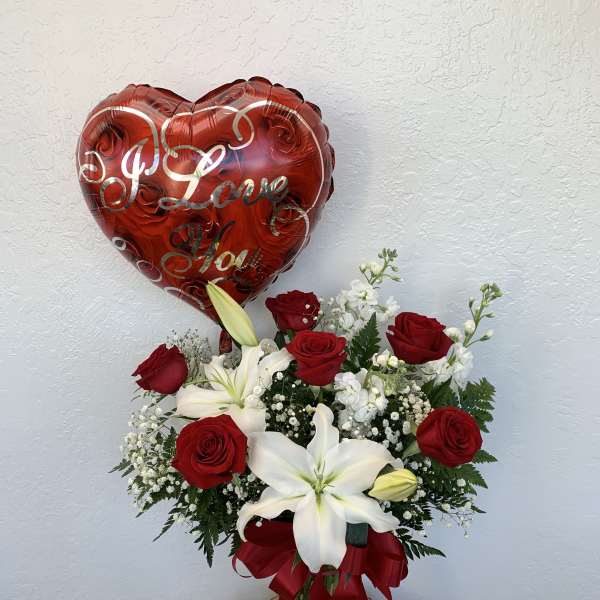 Red heart balloon above a bouquet of red roses and white lilies in a glass vase
