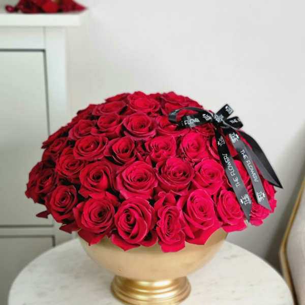 Round bouquet of red roses in a gold pedestal vase with a black ribbon