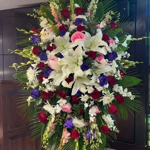 Large standing floral spray with white lilies, red and purple roses, and pink accents
