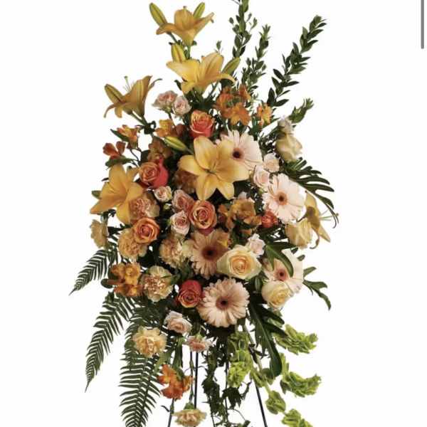 Tall floral standing spray with yellow lilies, peach roses, and pale gerbera daisies