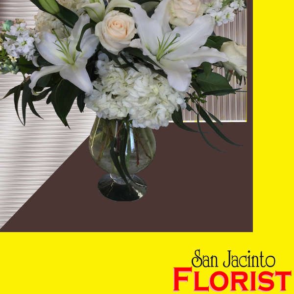 White lilies and roses arranged in a glass vase with blue flowers