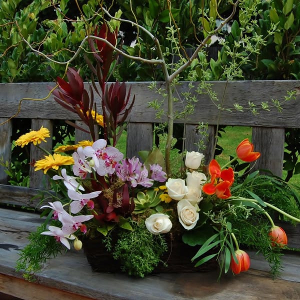 Mixed floral arrangement with orchids, roses, tulips, and yellow daisies