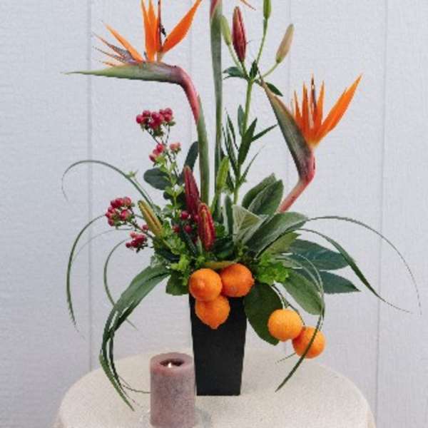 Tall tropical flower arrangement with orange bird-of-paradise blooms in a black vase