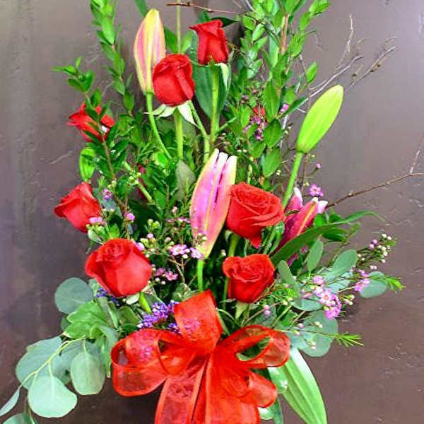 Tall bouquet of red roses and pink lilies in a glass vase with a red ribbon