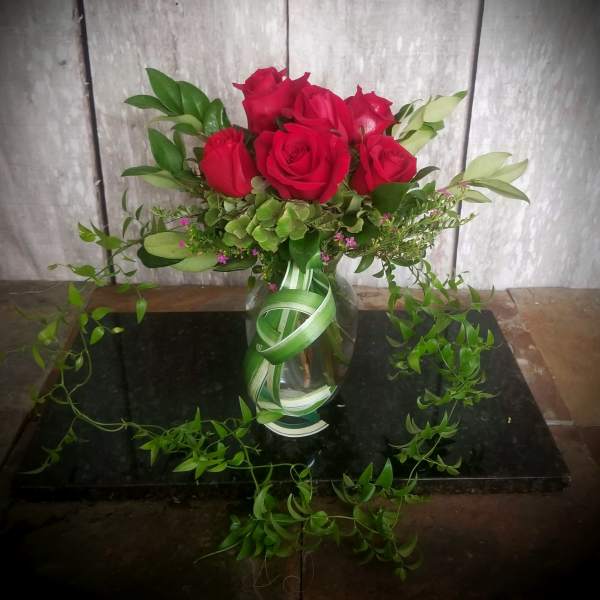Red roses in a clear glass vase with trailing greenery