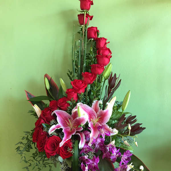 Tall arrangement of red roses and pink lilies in a black vase