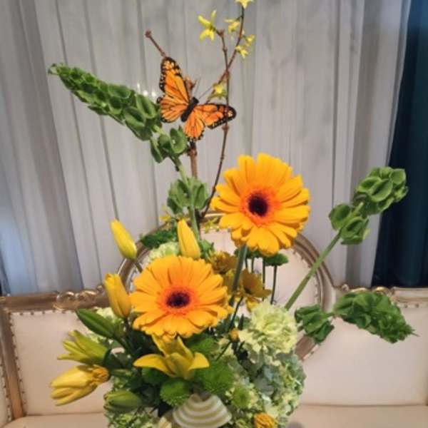 Yellow floral arrangement with orange gerbera daisies in a glass vase