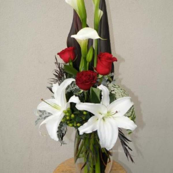 Tall bouquet of white calla lilies, white lilies, and red roses in a glass vase