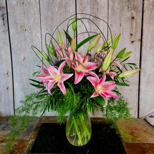 Pink lilies arranged in a clear glass vase with trailing greenery