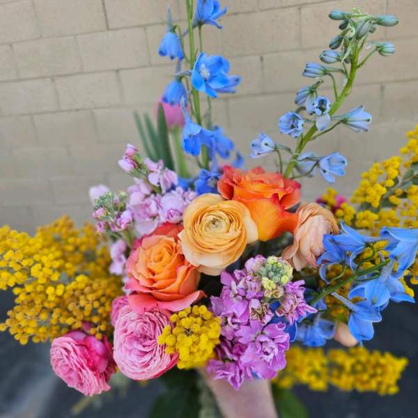 Handheld bouquet of orange and pink roses with blue and purple flowers