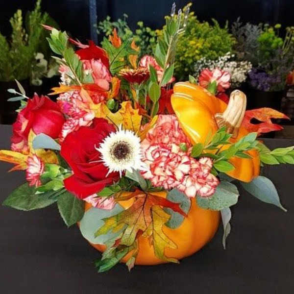 Autumn floral arrangement in a pumpkin-shaped container with red and orange blooms