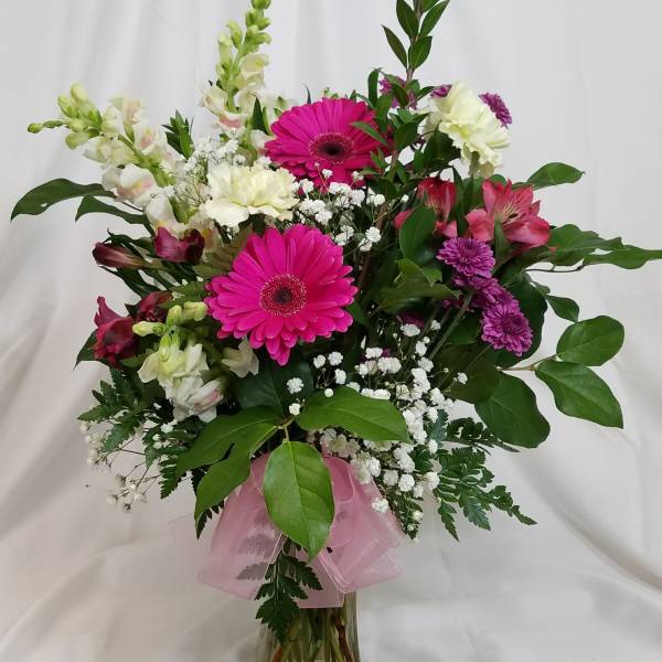 Mixed bouquet with pink gerbera daisies, white snapdragons, and purple blooms in a glass vase
