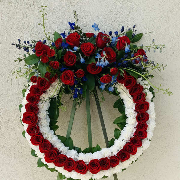 Standing floral wreath of red roses, white flowers, and blue accents on an easel