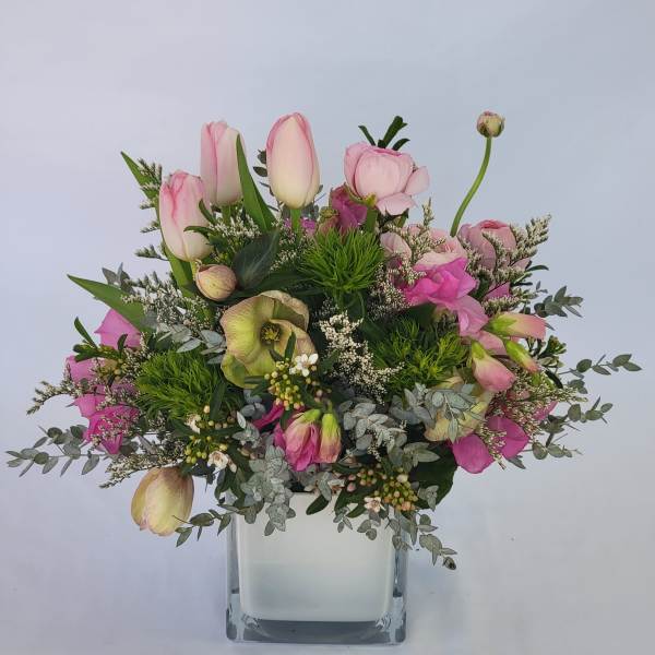 Pink tulips and mixed blooms arranged in a clear square vase