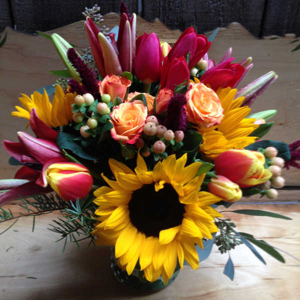 Bright mixed bouquet with sunflowers, tulips, and peach roses in a vase