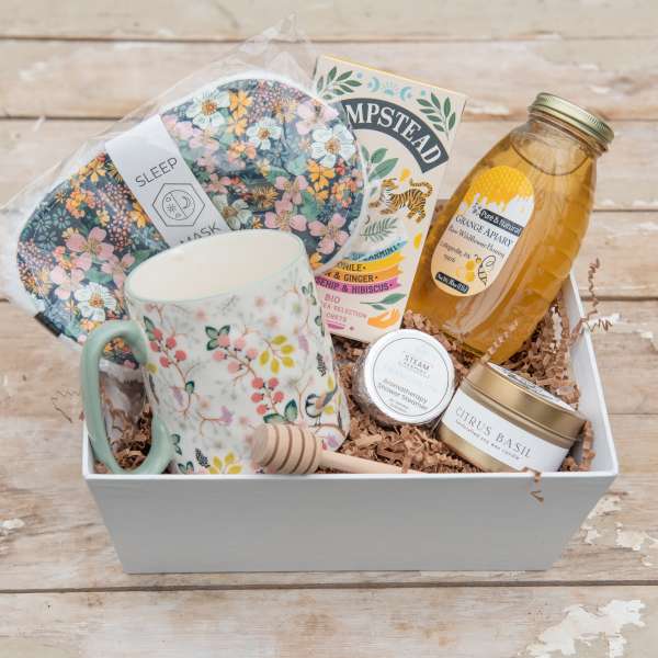 Gift basket with a floral mug, sleep mask, honey jar, candle, and shower steamer