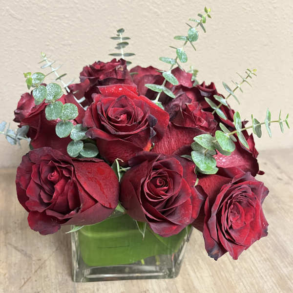 Red roses arranged in a square glass vase with eucalyptus stems