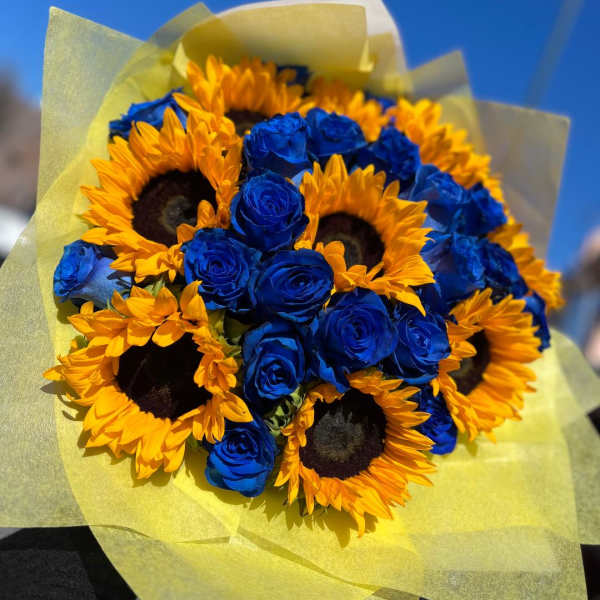 Bouquet of yellow sunflowers and blue roses wrapped in pale paper