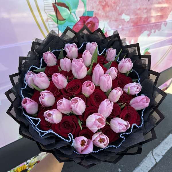 Bouquet of pink tulips and red roses wrapped in black paper