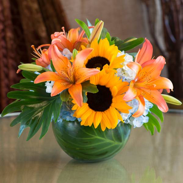 Bouquet of orange lilies and sunflowers in a green glass vase