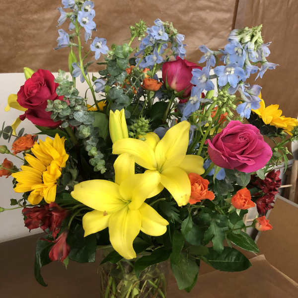 Mixed bouquet of lilies, roses, and blue delphinium in a glass vase