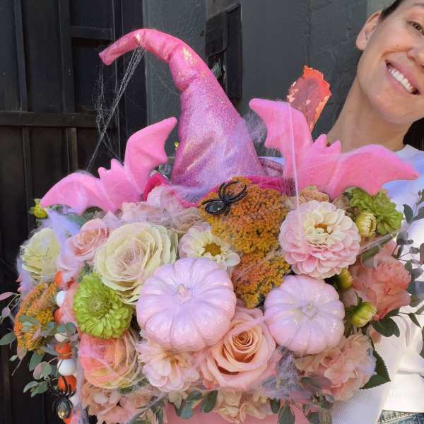 Pink pumpkin-shaped floral arrangement with roses, dahlias, and Halloween decorations