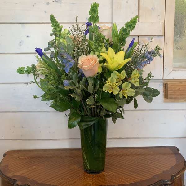 Mixed bouquet with roses, lilies, and blue flowers in a tall green vase