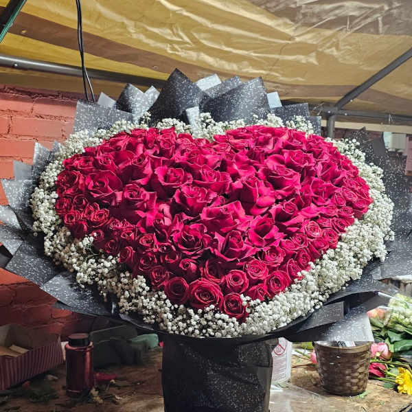 Heart-shaped bouquet of red roses edged with baby's breath in black wrap
